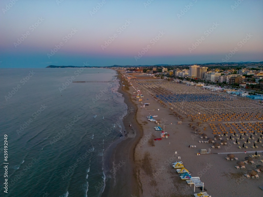 Italy, Rimini 15.08.2023: Beautiful sunset in Rimini. Drone photography of the city and the beach. Spectacular sunset on Adriatic coast. Vacation concept background. Rimini public beach. Panoramic sum