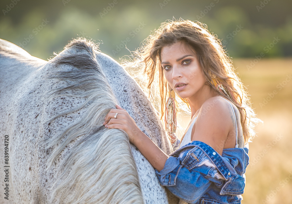 Beautiful blonde woman with curly hair with white hat and horse. Portrait of a girl with denim and her horse. Beautiful girl interacting and having fun with a horse at the ranch