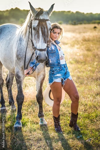 Beautiful blonde woman with curly hair with white hat and horse. Portrait of a girl with denim and her horse. Beautiful girl interacting and having fun with a horse at the ranch