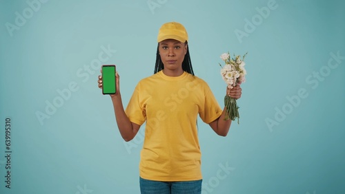 Delivery woman in uniform holding bouquet of flowers and smartphone, looking at the camera. Advertising area, workspace mockup. photo