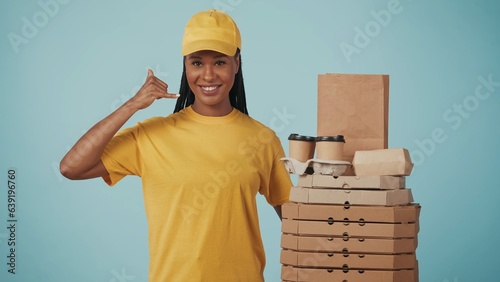 Delivery woman in uniform shows calling gesture, smiling at the camera. Isolated on blue background. photo