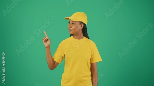 Delivery woman in uniform pointing at the empty area. Isolated on green background. Space to insert advertising.