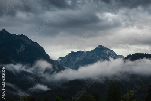 Nice misty fog in Alps mountain valley with storm sky. Austria landscape background