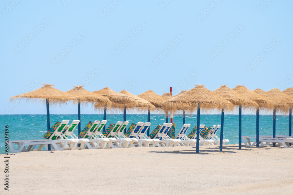 Beautiful sandy beach with palm tree umbrellas and sun loungers Beautiful sandy beach with palm tree umbrellas and sun loungers