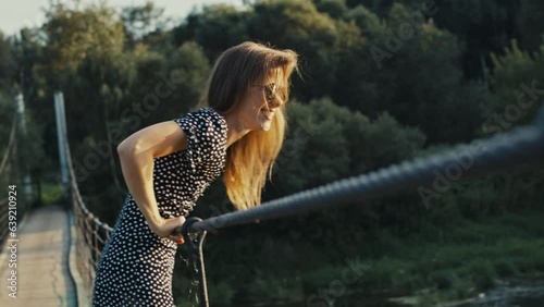 A beautiful young slender girl spits from a suspension bridge. photo