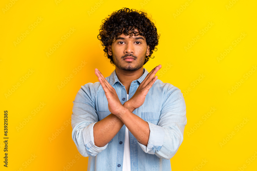 Portrait of serious confident man with wavy hairstyle wear jeans shirt arms crossed show deny gesture isolated on yellow color background