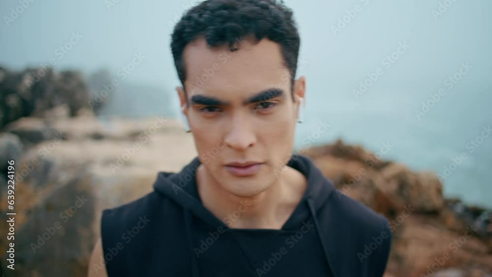 Male athlete looking camera at cloudy seaside closeup. Handsome fit guy listen Male athlete looking camera at cloudy seaside closeup. Handsome fit guy listen