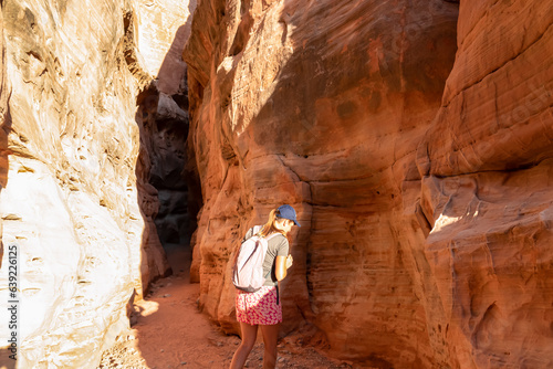 Woman walking in the narrow Kaolin Wash slot canyon along White Domes Hiking Trail in Valley of Fire State Park in Mojave desert, Nevada, USA. Massive cliffs of striated red and white rock formations