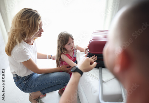 Upset sad little girl is packing suitcase with parents. Family separation for kids concept photo