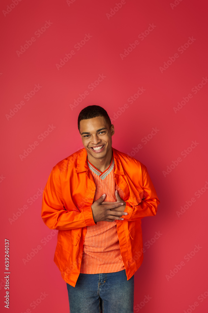 glad african american man touching chest, smiling at camera on red, grateful gesture, orange shirt glad african american man touching chest, smiling at camera on red, grateful gesture, orange shirt