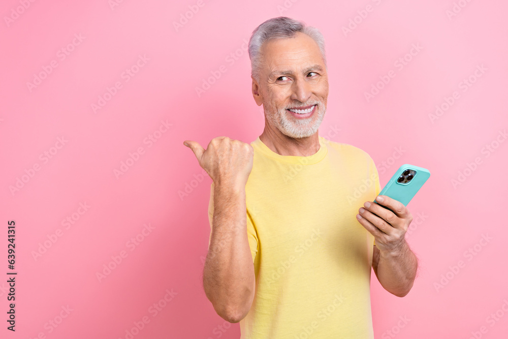Photo of good mood man dressed yellow t-shirt hold smartphone directing look at offer empty space isolated on pink color background Photo of good mood man dressed yellow t-shirt hold smartphone directing look at offer empty space isolated on pink color background