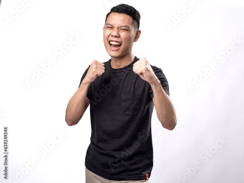 A portrait of an Asian man wearing a black t-shirt,  posing in a boxing stance as if about to throw a punch, isolated on a white background. © Daniel