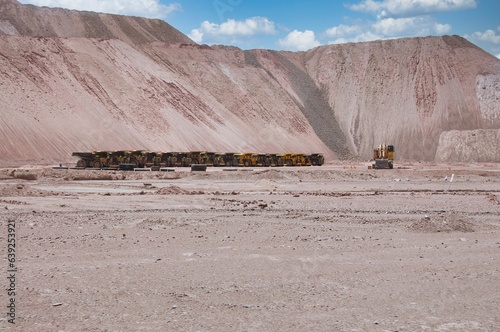 Big yellow mining trucks parked in a row in front of a big hill. Mining trucks in Atacama desert, Chile. Lithium mining industry in Chile. Big mining trucks and diggers waiting for their next use. 
