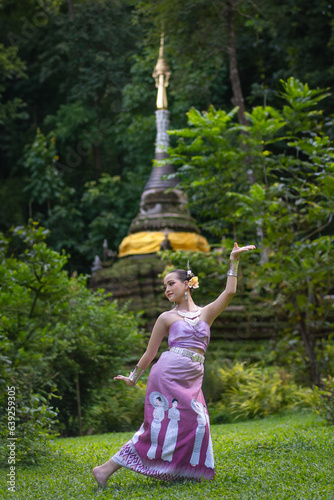 Pretty girl wearing beautiful traditional Thai dresses with the Thai Dance show in green natural at Wat Pha Lat Temple the famous place in Chiang Mai, Thailand.