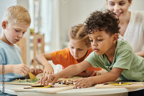 african american kid playing with didactic material near children and teacher in montessori school