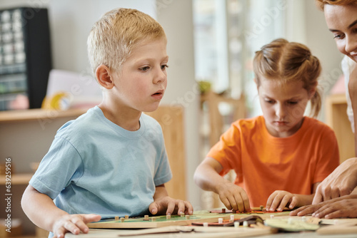 boy sitting near teacher and didactic materials during lesson in montessori school