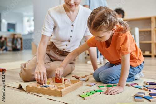 montessori school concept, girl playing color matching game near female teacher, sitting on floor photo