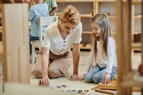 montessori material, smart girl playing educational game with blonde teacher, early school education © LIGHTFIELD STUDIOS