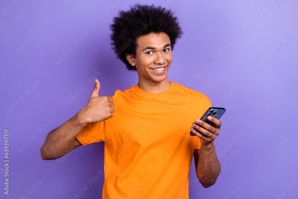 Photo of handsome cheerful guy hold smart phone hand finger demonstrate thumb up isolated on violet color background Photo of handsome cheerful guy hold smart phone hand finger demonstrate thumb up isolated on violet color background