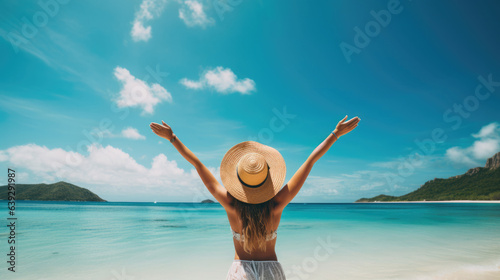 Summer vacation happy carefree joyful bikini woman arms outstretched in happiness enjoying tropical beach destination. Holiday girl sitting with sun hat relaxing from behind on Caribbean vacation. © Sasint