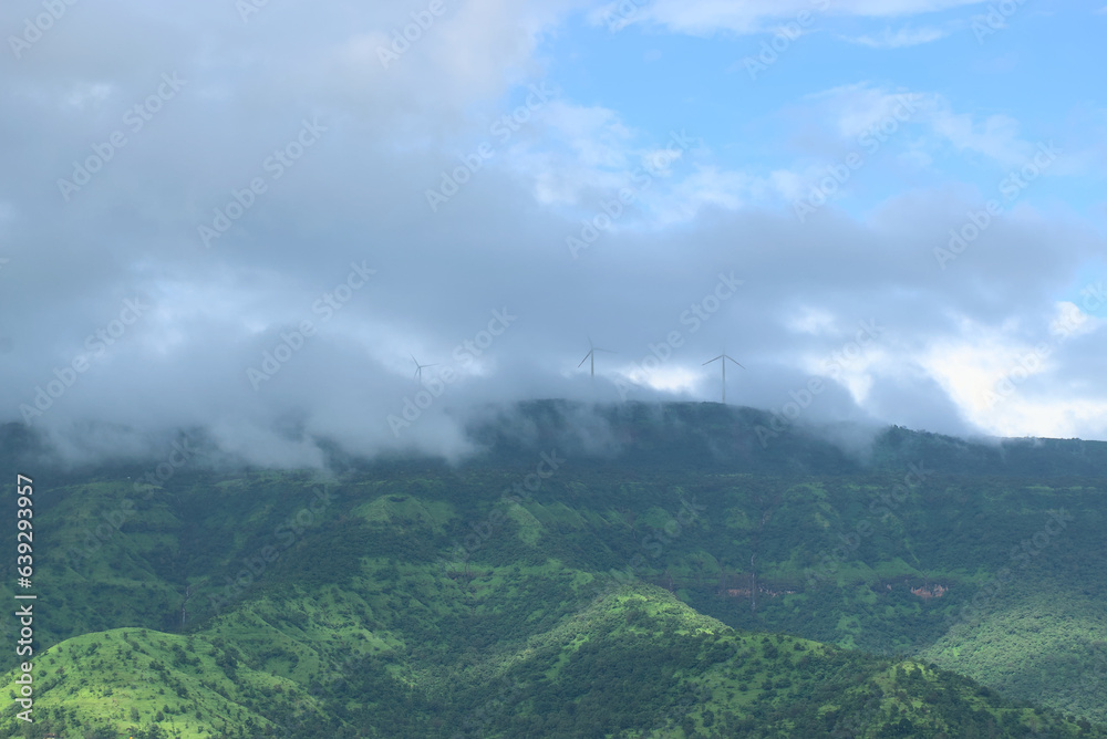Panoramic landscape view of beautiful lush green Sahyadri mountains with windmills visible through clouds on the top at Tapola, Maharashtra, India