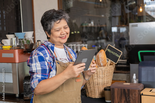 Happy aging society people lifestyle with modern technology tablet concept, Healthy Asian senior elderly retired woman cafe coffee small business owner using tablet receive customer order management
