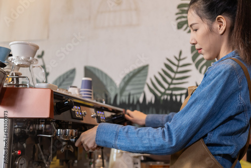 Side view, young attractive Asian barista female using professional coffee machine to make hot espresso coffee to mug in cozy cafe, small business owner start-up for young people lifestyle concept