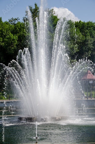 A pond with working fountains  surrounded by a monument of trees and lawn