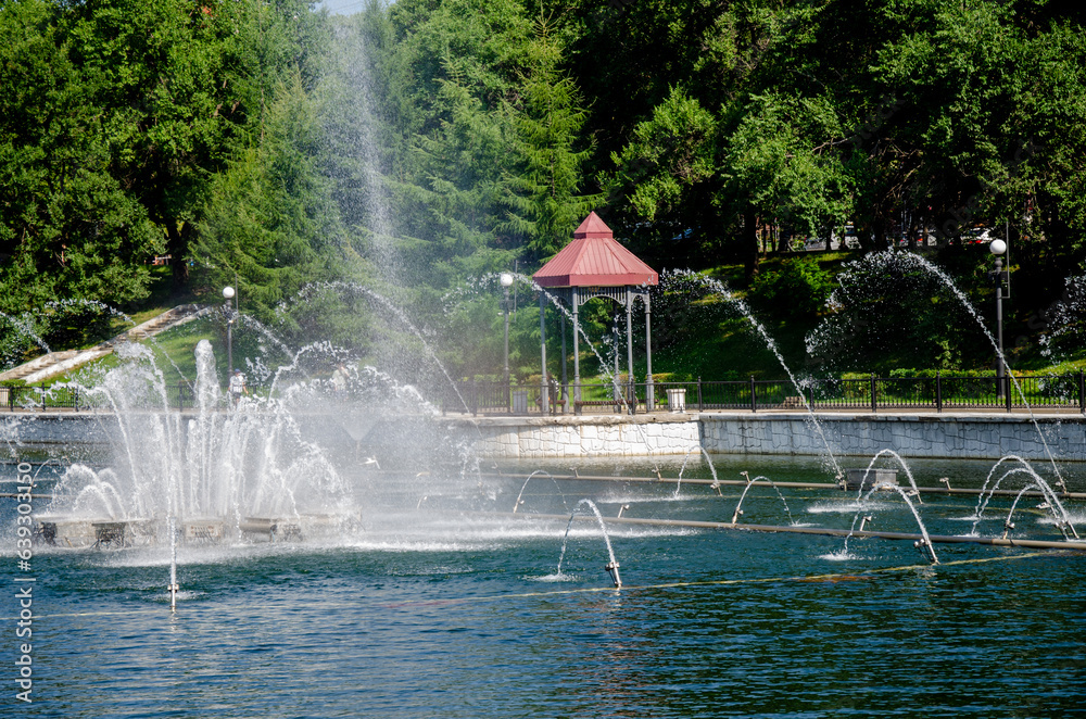 Fototapeta premium A pond with working fountains, surrounded by a monument of trees and lawn
