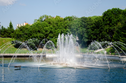 A pond with working fountains  surrounded by a monument of trees and lawn