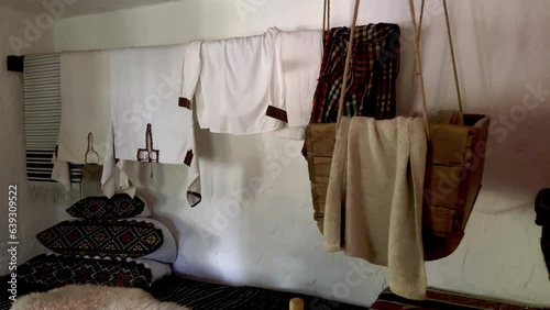 Cosiness Ukrainian ethno house interior room. Embroidered national clothes hanging on the rope. Baby's cradle swings.  photo