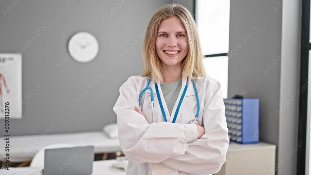 Young blonde woman doctor smiling confident standing with arms crossed gesture at clinic Young blonde woman doctor smiling confident standing with arms crossed gesture at clinic