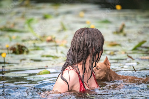 Fototapeta Naklejka Na Ścianę i Meble -  A beautiful dark-haired girl swims in the river with a pit bull terrier dog.