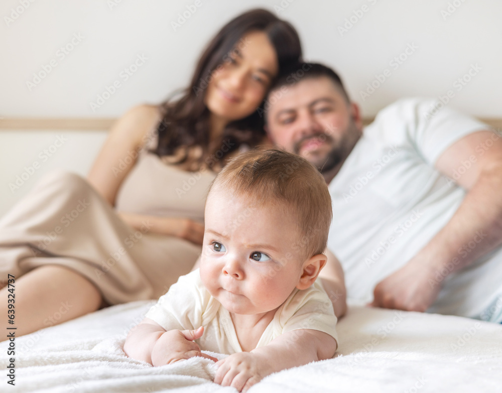 happy young family with baby infant kid boy sitting on bed, cuddling kissing child on hand, cheek, caresses. traditional family lying on bed at home.woman man kid portrait,posing in bedroom happy young family with baby infant kid boy sitting on bed, cuddling kissing child on hand, cheek, caresses. traditional family lying on bed at home.woman man kid portrait,posing in bedroom