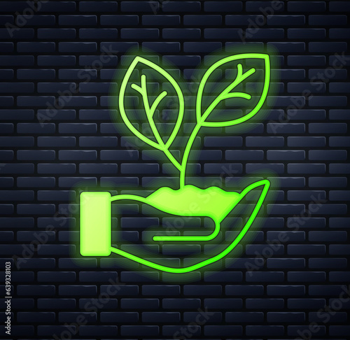 Glowing neon Hand hold a leaf of the plant icon isolated on brick wall background. Care nature. Leaf shoots with environmental protection. Vector