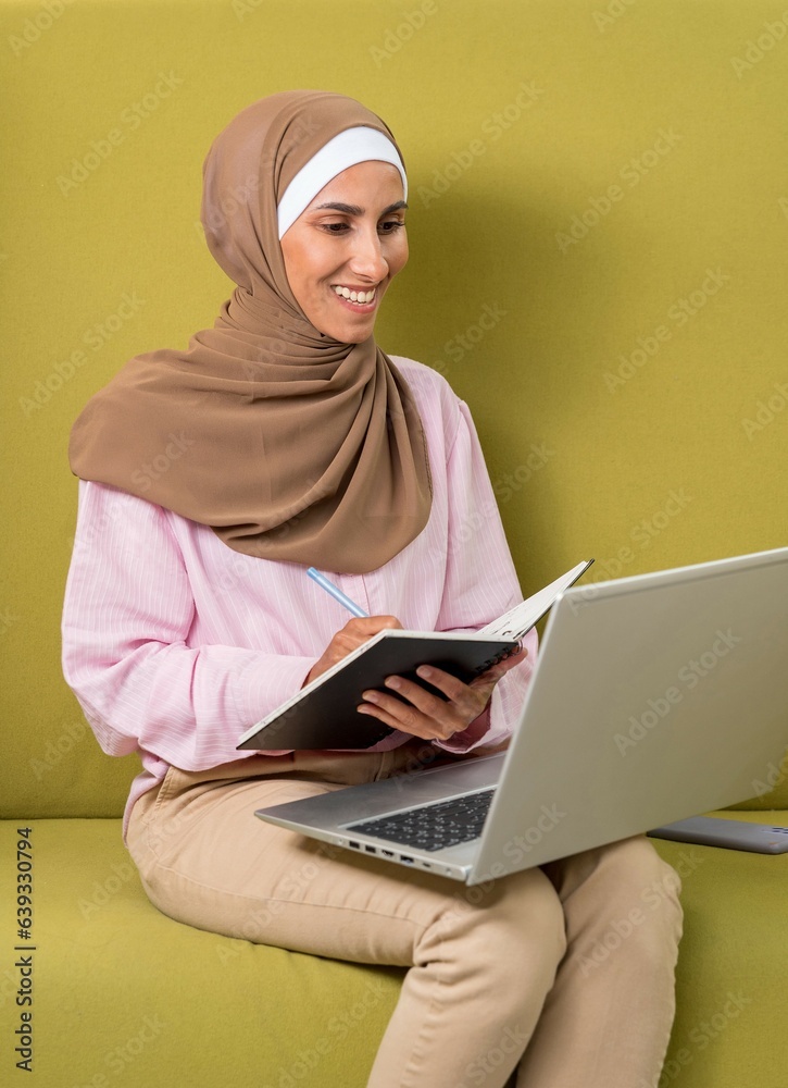 Vertical photo. Arab lady in hijab, data research plan on note in MBA college class in sales report, remote work in free space on laptop. Happy consultant, lifestyle, coworking. Green background Vertical photo. Arab lady in hijab, data research plan on note in MBA college class in sales report, remote work in free space on laptop. Happy consultant, lifestyle, coworking. Green background