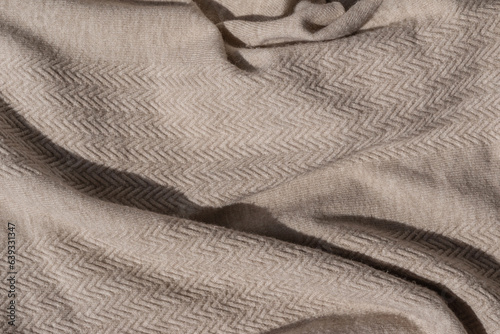 Messy crumpled neutral light brown or taupe knitted sweater texture with sunlight and shadow. Soft woolen jersey knitwear fabric background
