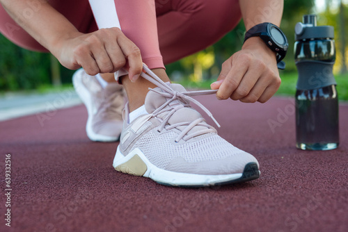 Fototapeta Naklejka Na Ścianę i Meble -  Closeup of woman tying shoe laces. Female sport fitness runner getting ready for jogging outdoors