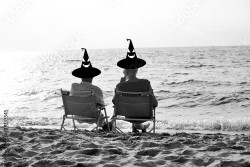 Halloween concept Witch Hat Halloween costume senior couple at Sunset: Silhouette Lover resting and sitting on the beach together, black and white , Halloween celebration concept