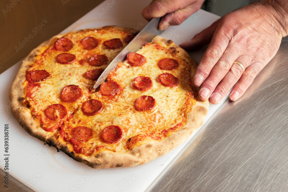 A chef cuts freshly baked pizza just out of the hot oven, A chef cuts freshly baked pizza just out of the hot oven,