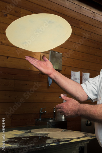 A skillful chef is preparing pizza, twirling the dough, making thin crust for delicious Italian pizza in an upscale restaurant
