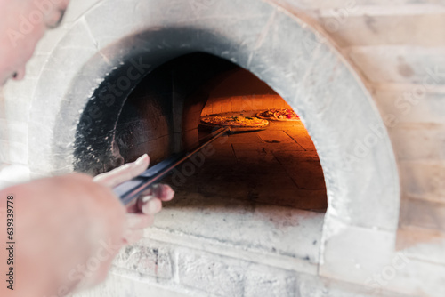 A talented French chef places a cheese and sausage pizza into the hot oven for 5 minutes