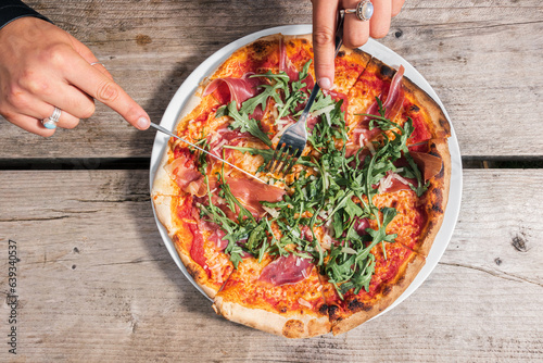 A girl cuts a delicious herb-topped pizza served by a waiter at a homey cafe