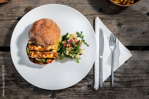 A burger and a salad on a white plate at an outdoor café on a wooden table, clean cutlery and napkin