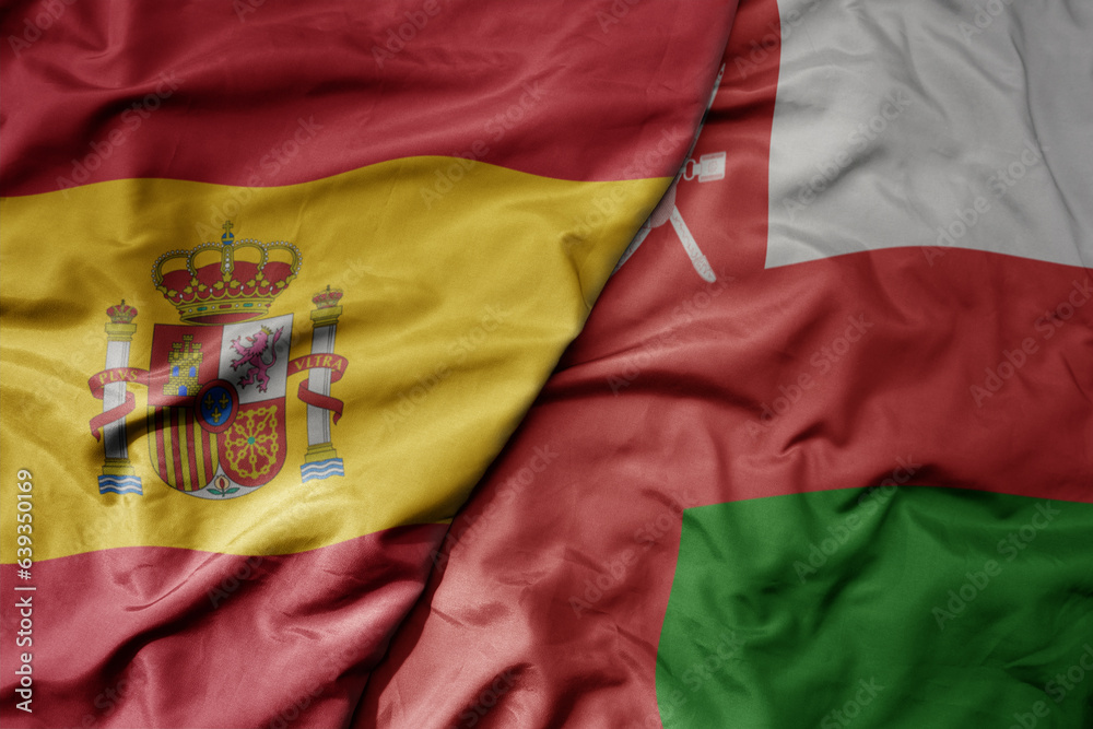 big waving national colorful flag of spain and national flag of oman . big waving national colorful flag of spain and national flag of oman .