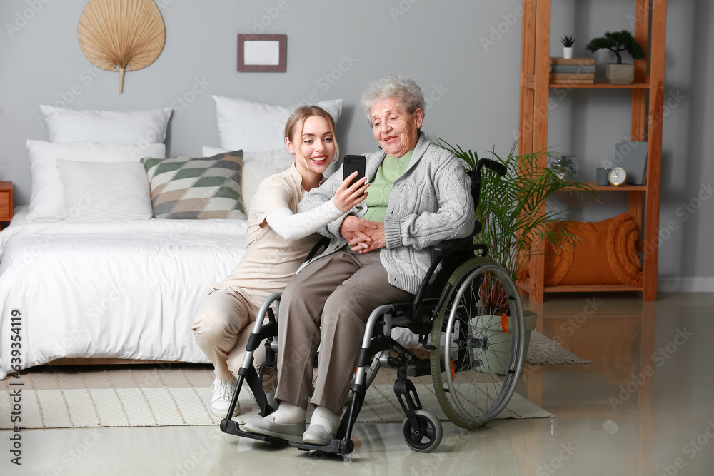 Young caregiver with senior woman in wheelchair using mobile phone at home Young caregiver with senior woman in wheelchair using mobile phone at home