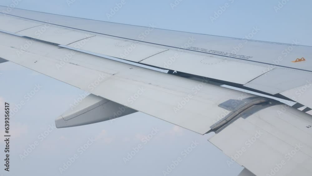 view through aircraft window with plane's wing over blue sky with white fluffy clouds from airplane flight fly over the clouds in a sunny day with cloud moving
