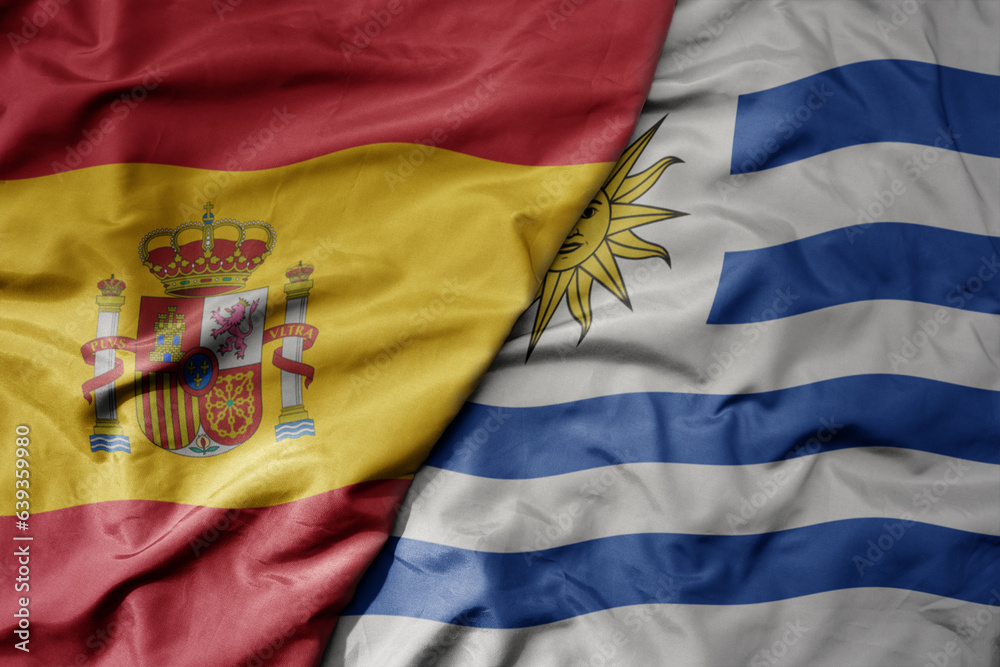 Fototapeta premium big waving national colorful flag of spain and national flag of uruguay .
