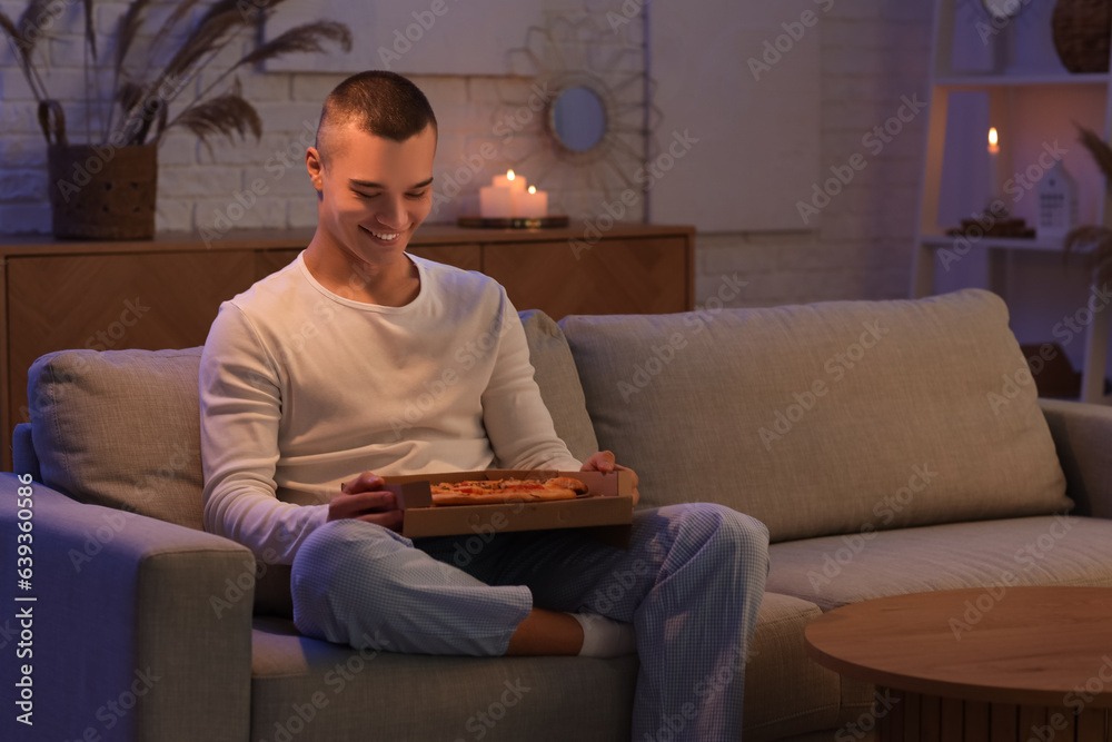 Hungry young man with tasty pizza at home late in evening