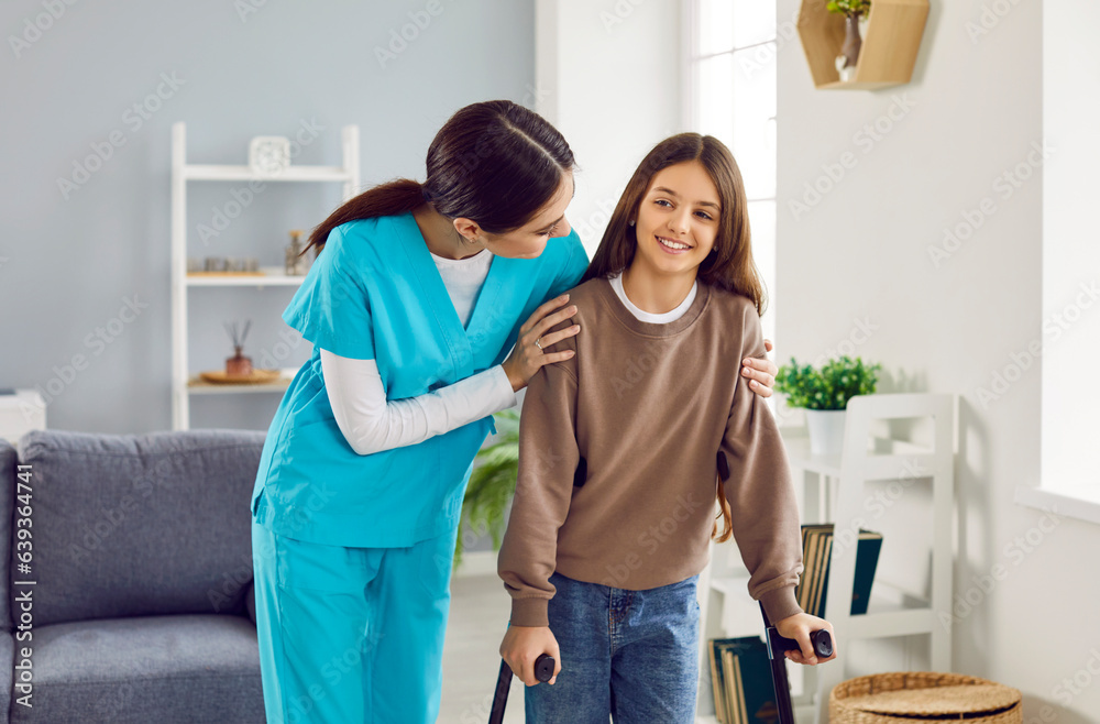 Obraz premium Friendly woman doctor, nurse or caregiver in uniform helps happy child patient girl with broken leg walk with orthopedic crutches at home. Injury, rehabilitation concept